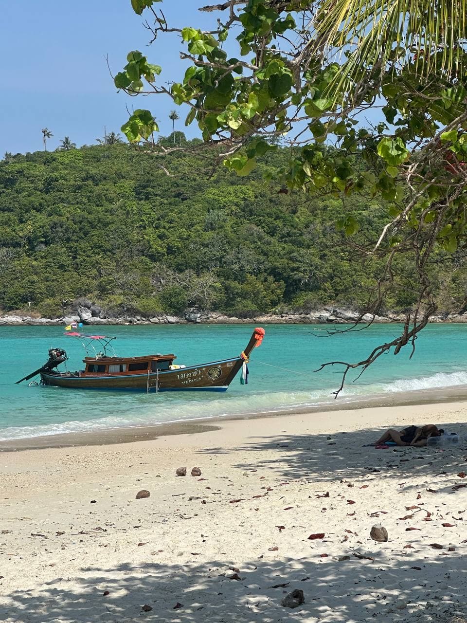 Longtail boat beside a quiet beach and green hillside